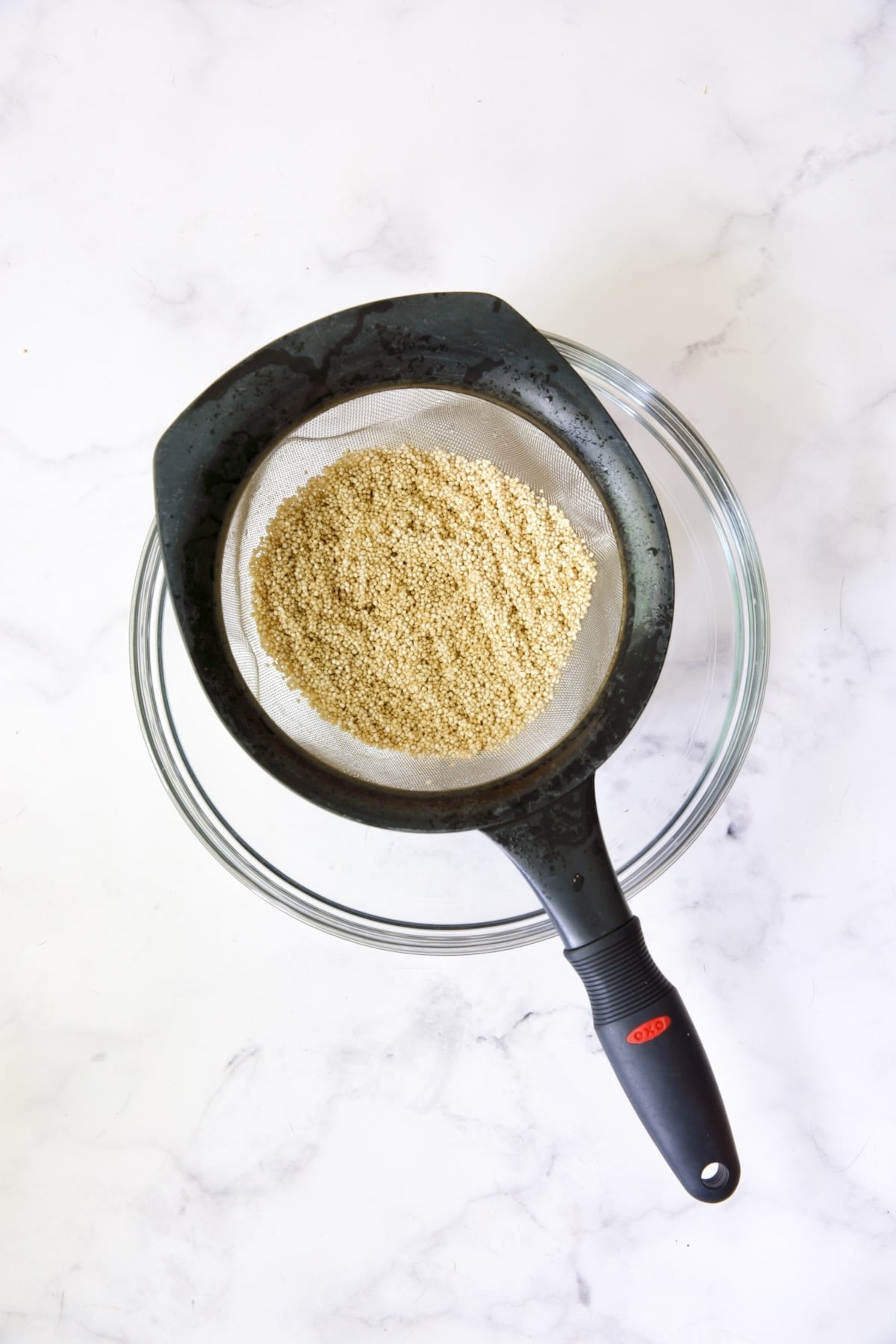 Quinoa in sieve set over a glass bowl.