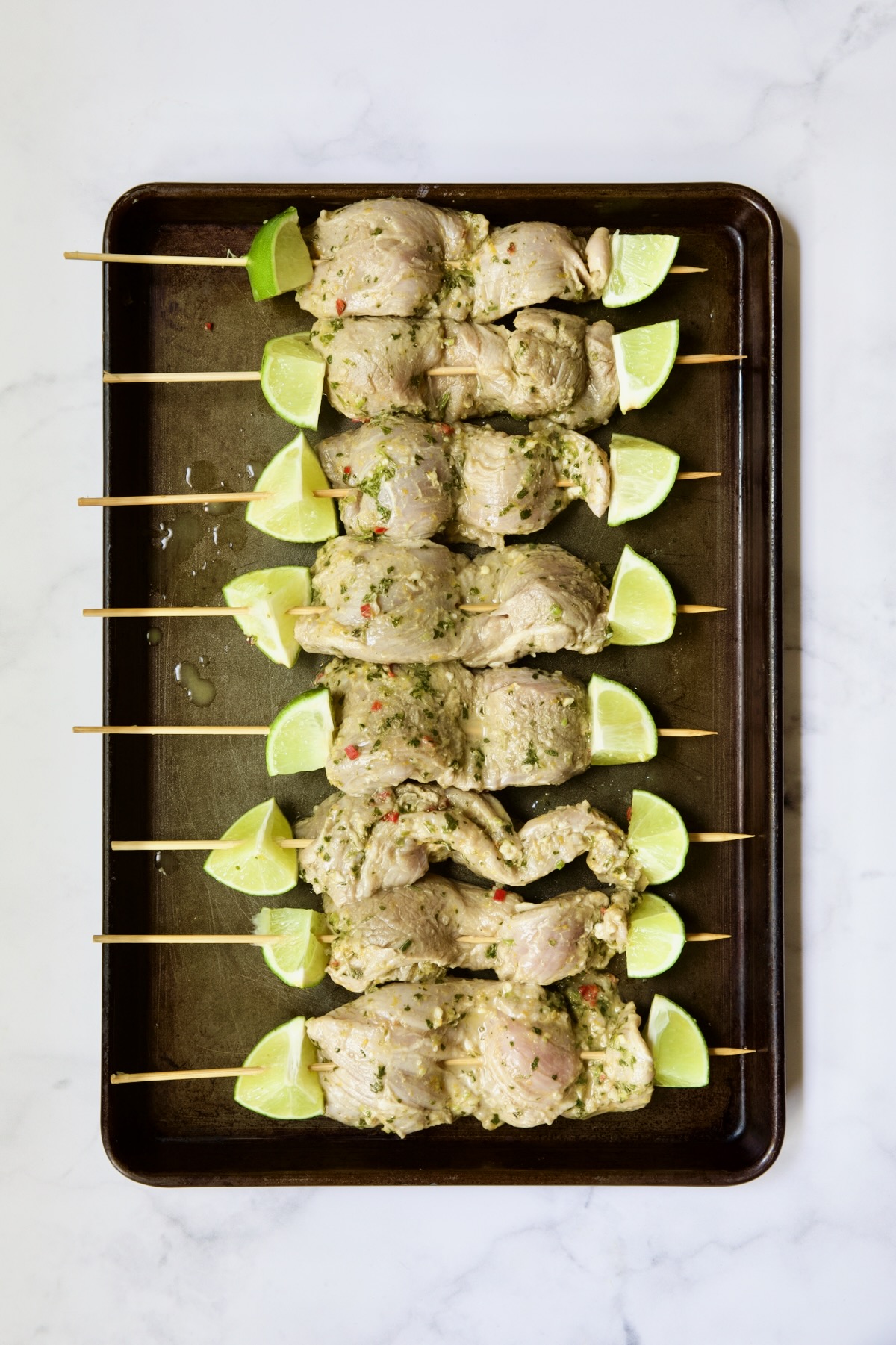 Uncooked pork tenderloin skewers on rimmed baking sheet.