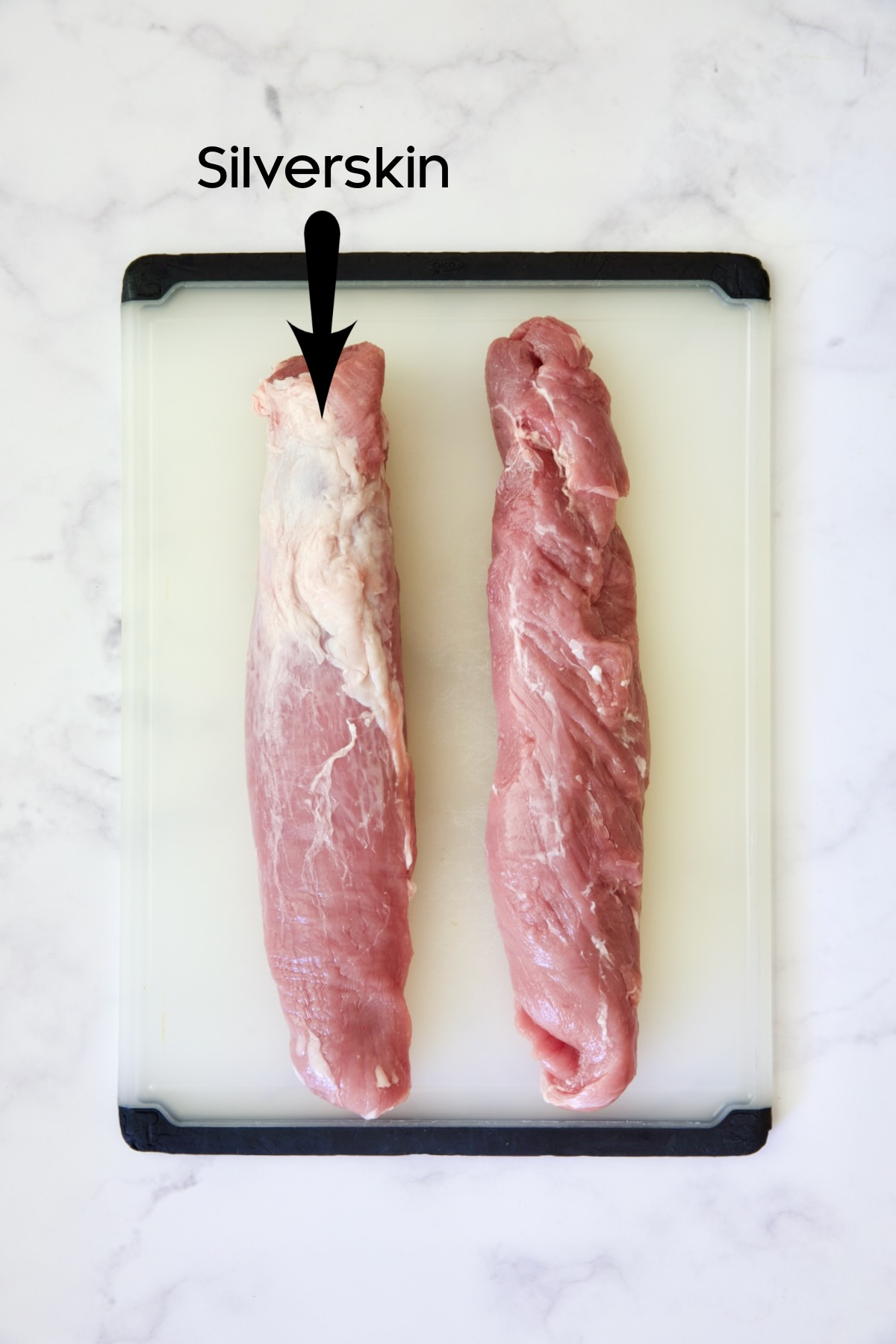 Two pork tenderloins on white plastic cutting board, one trimmed the other untrimmed.