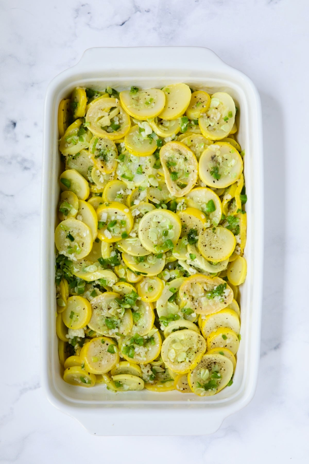 Yellow squash in white baking dish before mayonnaise and egg mixture is added.