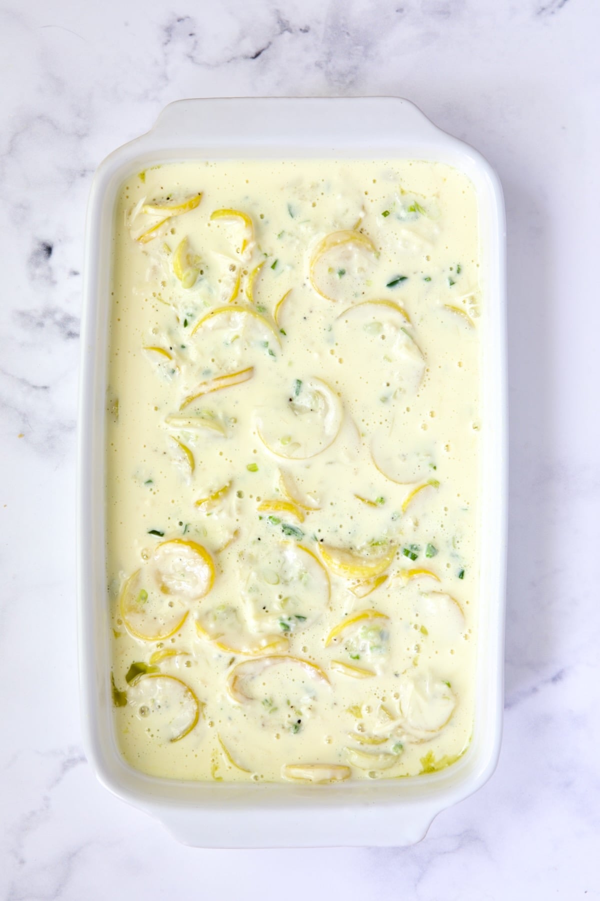 Squash casserole in white baking dish before cracker topping is added.