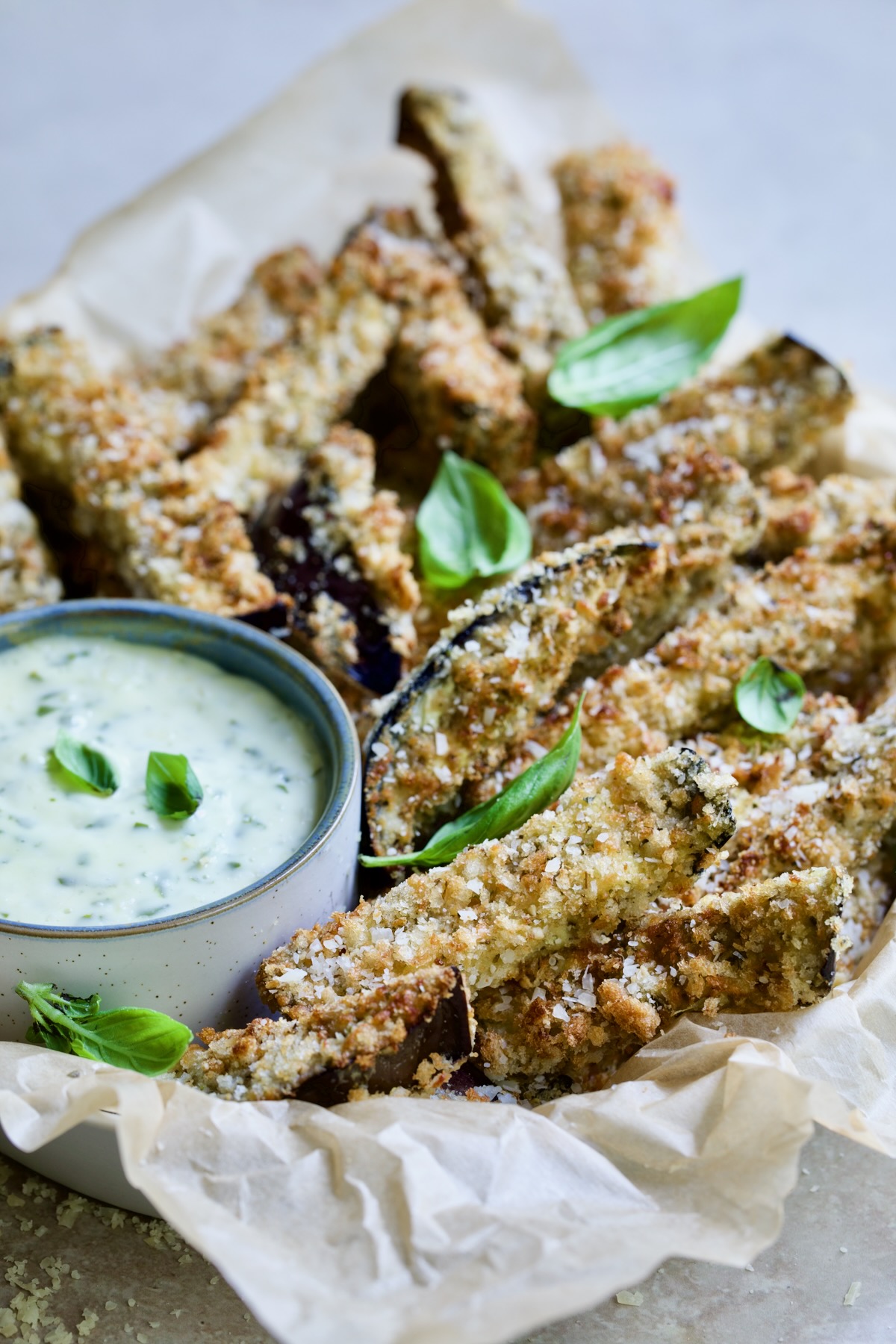 Air Fryer Eggplant Fries with Garlic Basil Aioli in parchment lined basket garnished with fresh basil.