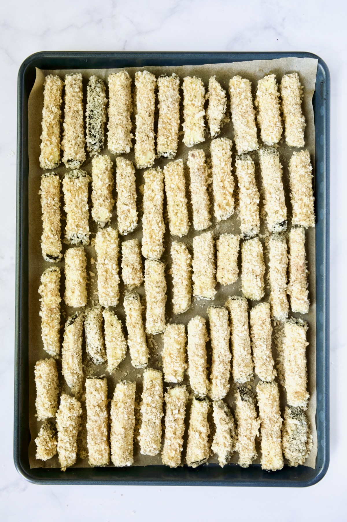 Breaded eggplant fries on parchment paper-lined rimmed baking sheet.