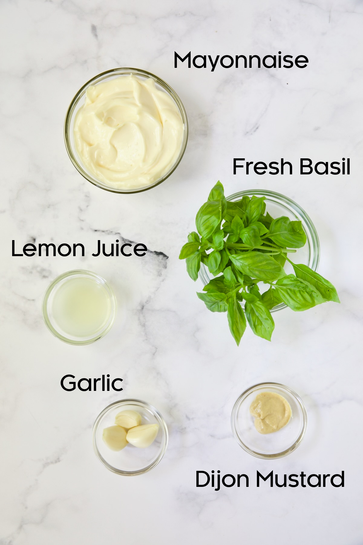 Ingredients for Garlic Basil Aioli in glass bowls on white background.