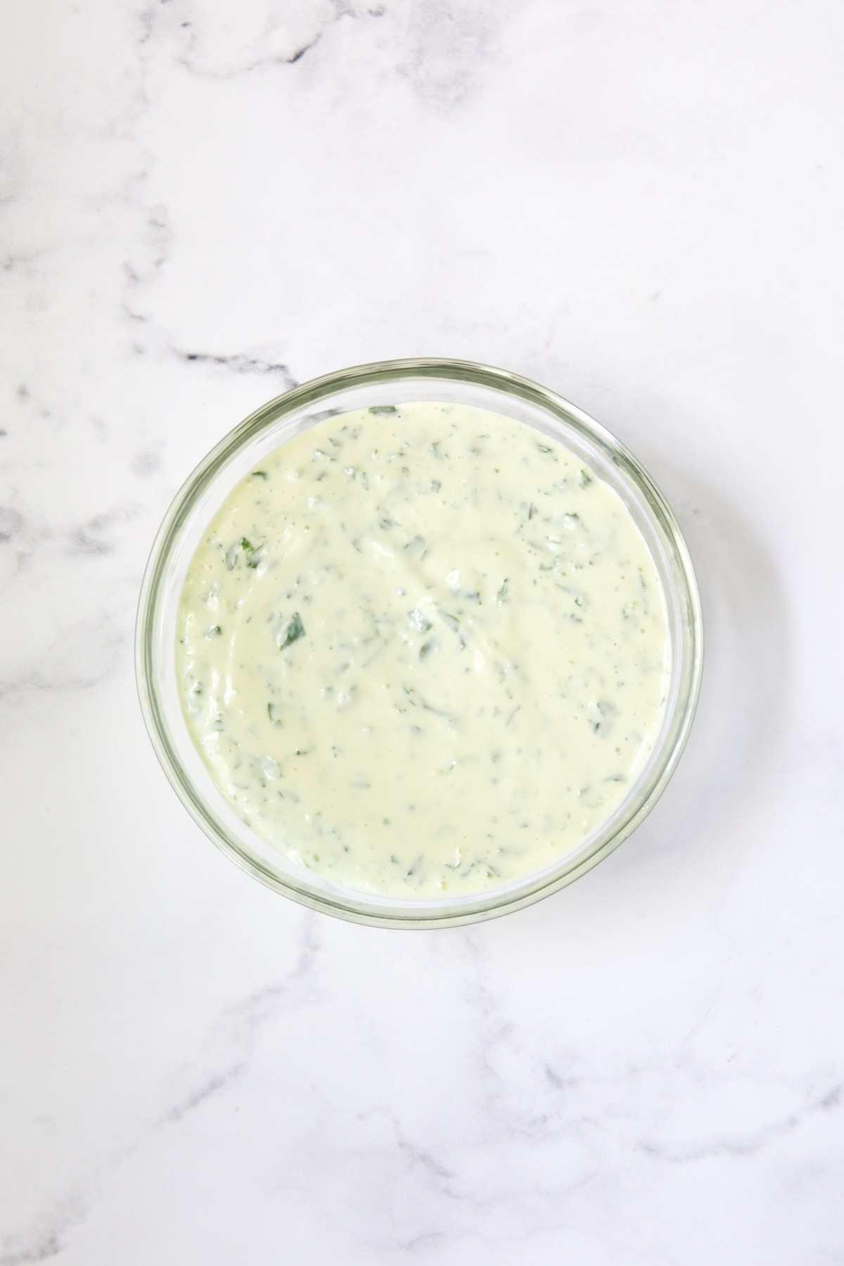 Bowl of Garlic Basil Aioli on marble surface.