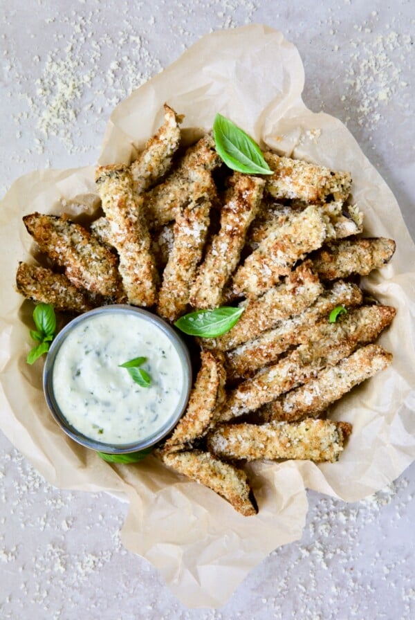 Air Fryer Eggplant Fries with Garlic Basil Aioli in basket with parmesan cheese and fresh basil leaves.