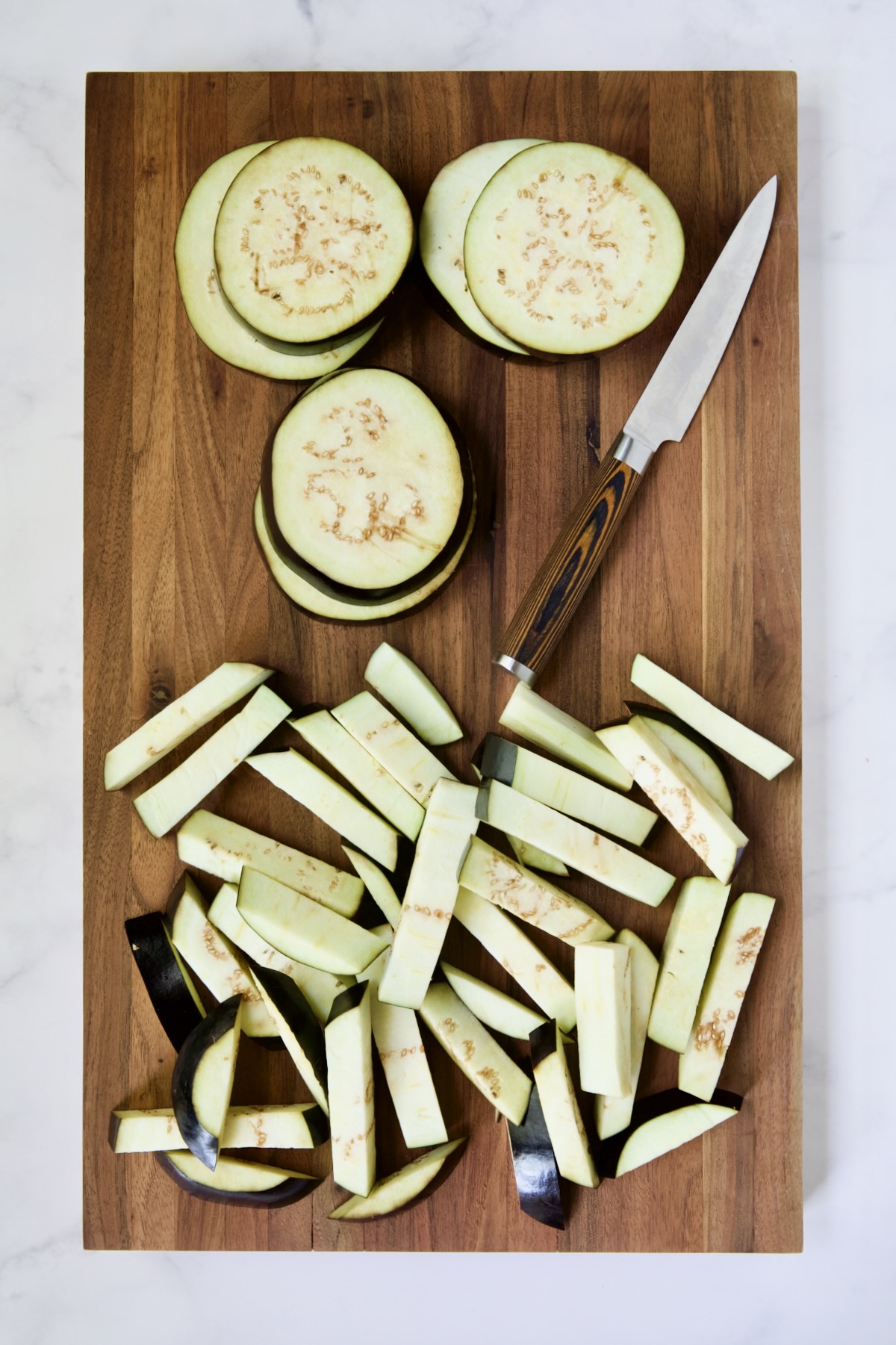 Eggplant rounds and fries on wood cutting board with knife.