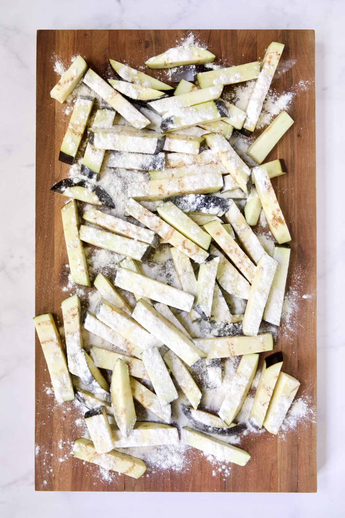 Eggplant fries on wood cutting board dusted with all-purpose flour.