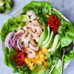 Butter Lettuce Salad with Shrimp, Mango and Avocado on platter with serving utensils.