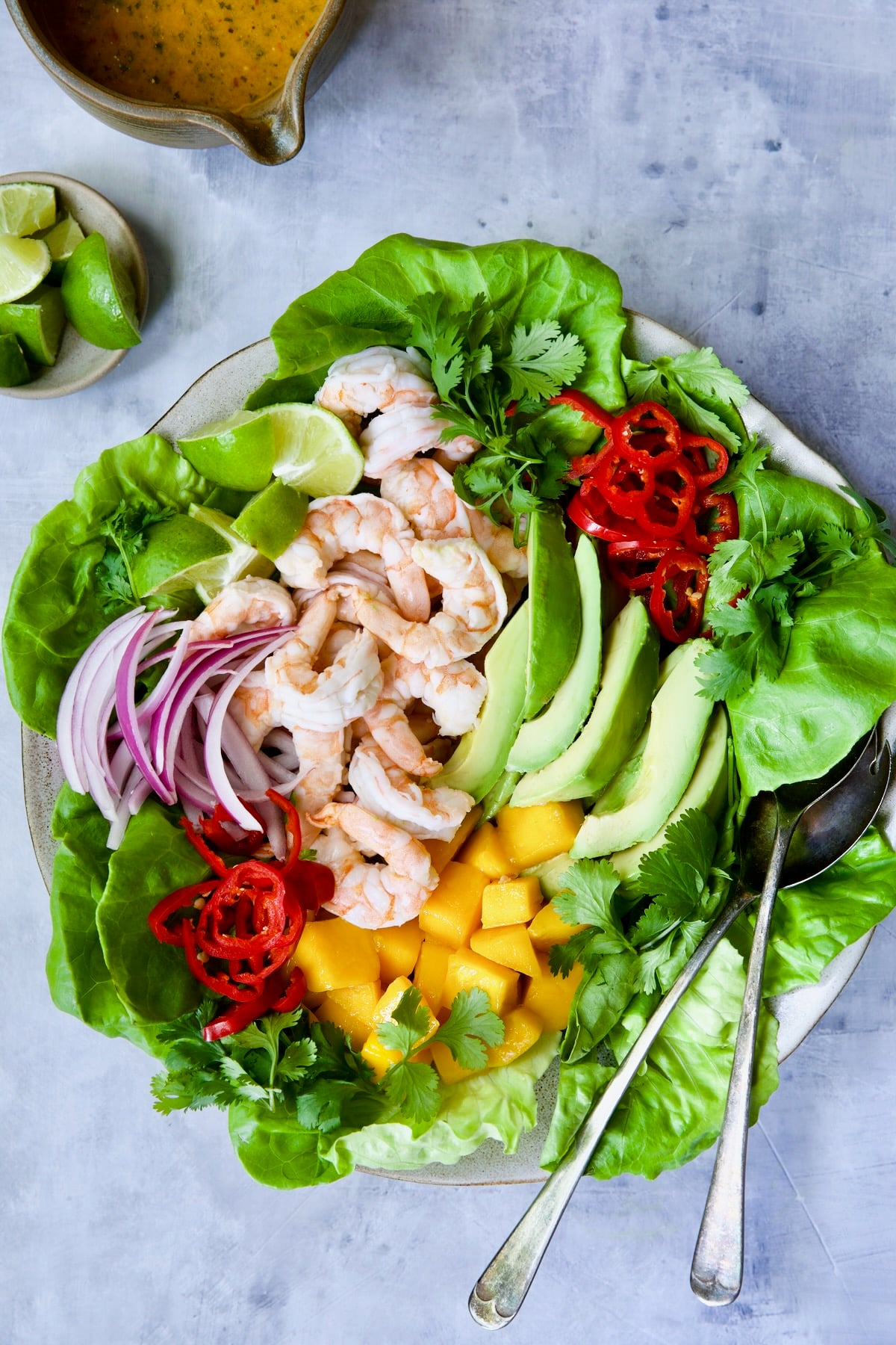 Butter Lettuce Salad with Shrimp, Mango and Avocado on platter with serving utensils.
