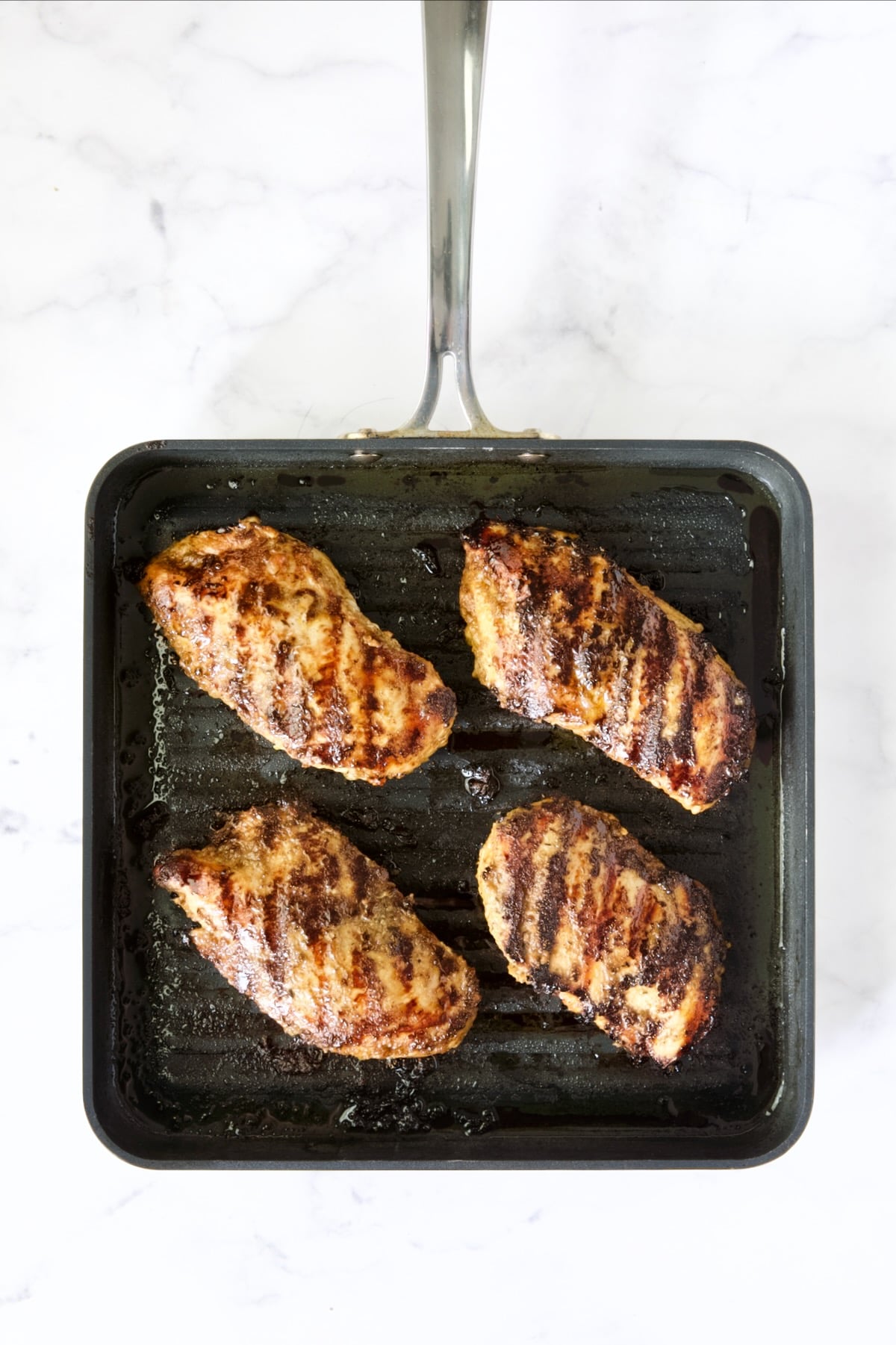 Four grilled chicken breasts on grill pan.