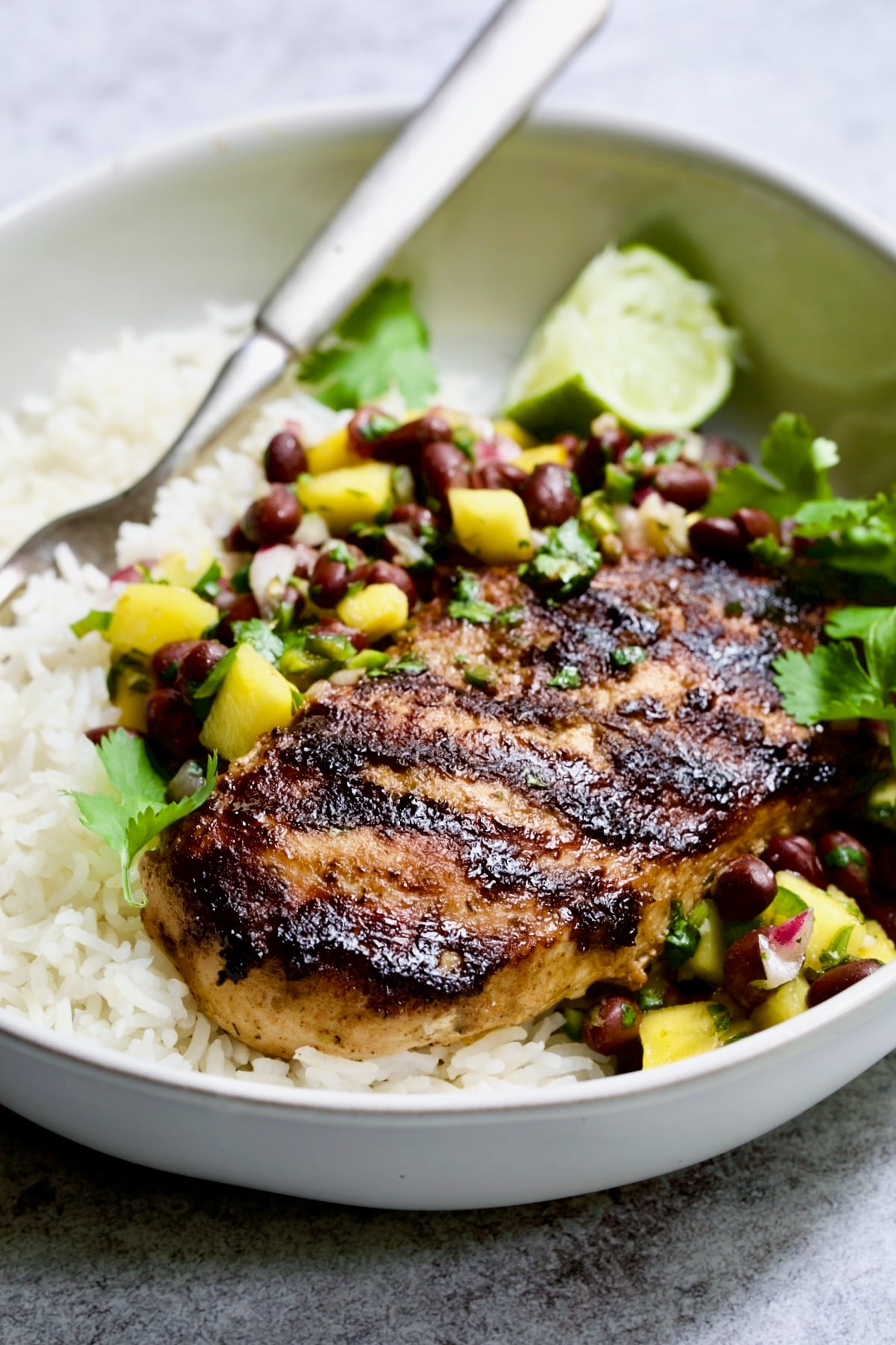 Caribbean Jerk Chicken with Mango Black Bean Salsa with rice in white bowl.