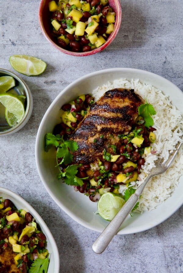 Caribbean Jerk Chicken with Mango Black Bean Salsa in white bowl garnished with cilantro and squeezed lime wedges.