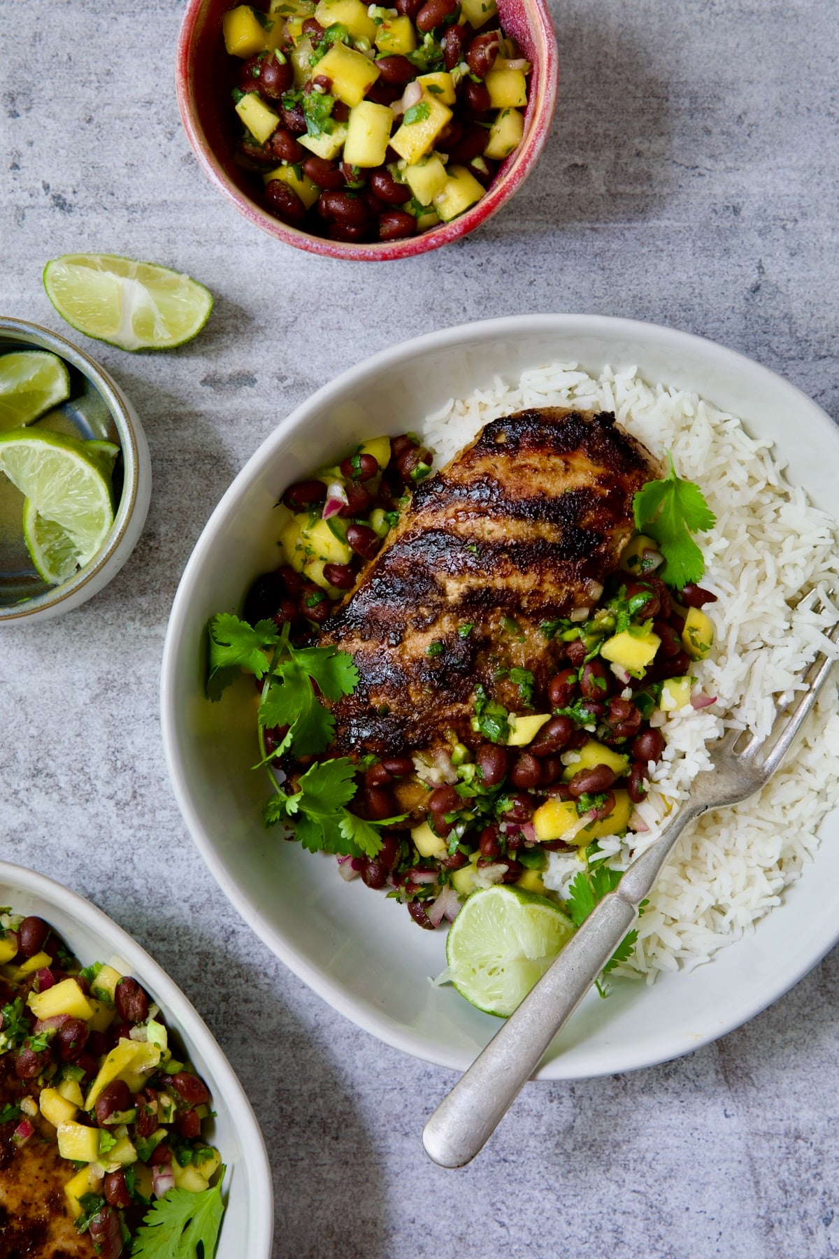 Caribbean Jerk Chicken with Mango Black Bean Salsa in white bowl garnished with cilantro and squeezed lime wedges.
