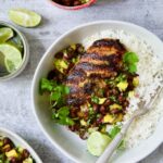 Caribbean Jerk Chicken with Mango Black Bean Salsa in white bowl garnished with cilantro and squeezed lime wedges.