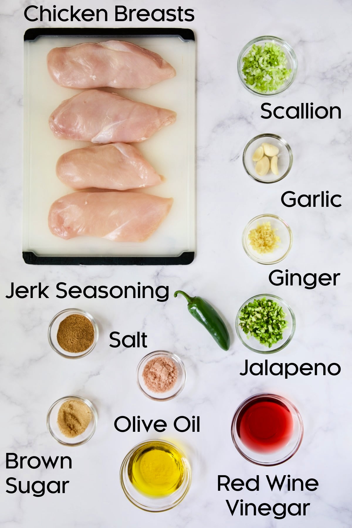 Ingredients for Caribbean Jerk Chicken on glass bowls and four uncooked chicken breasts on white cutting board.
