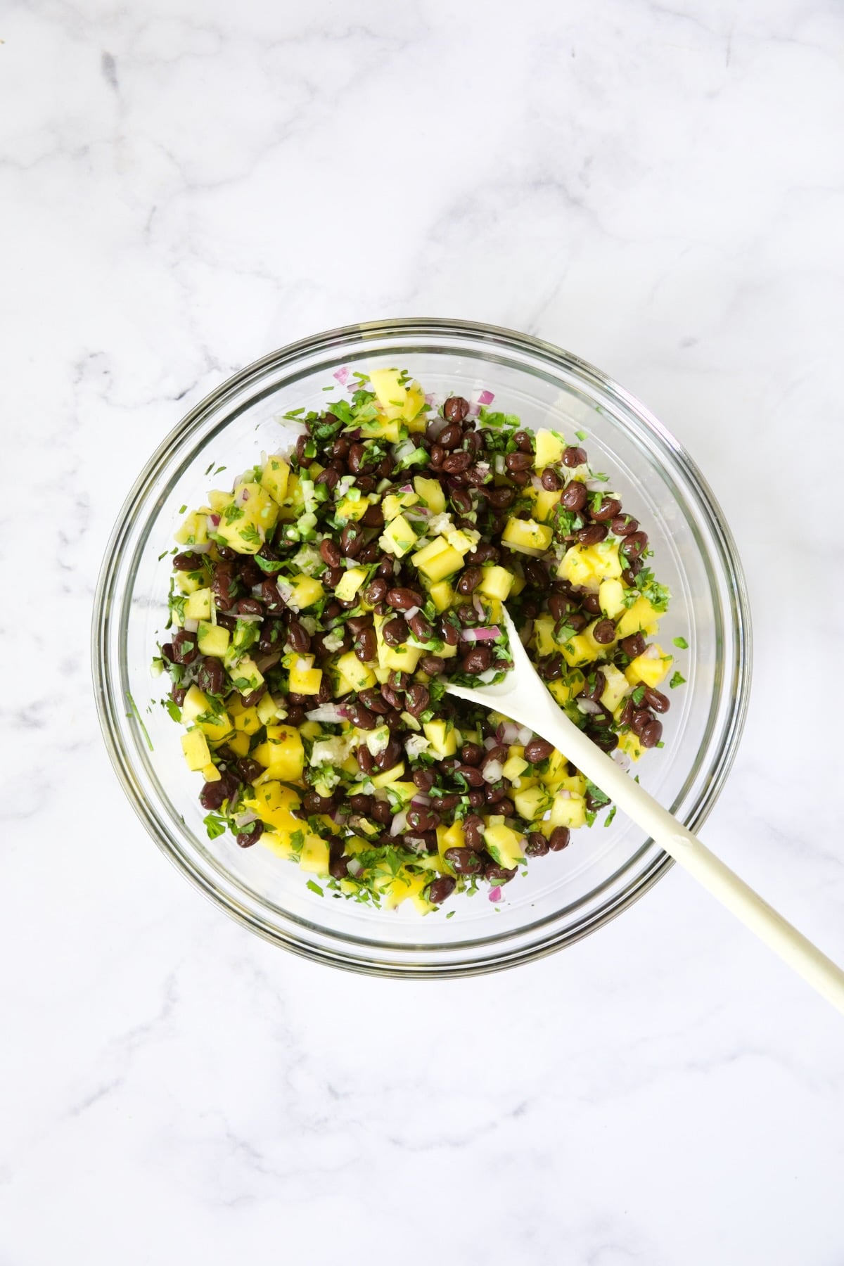 Black Bean Mango Salsa in glass bowl being stirred with white spoon.