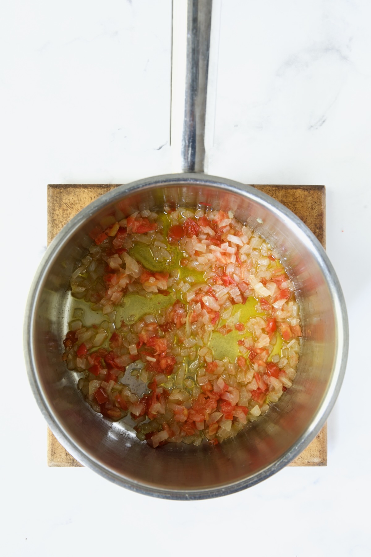 Cooked onions and tomatoes in stainless steel saucepan on wood trivet.