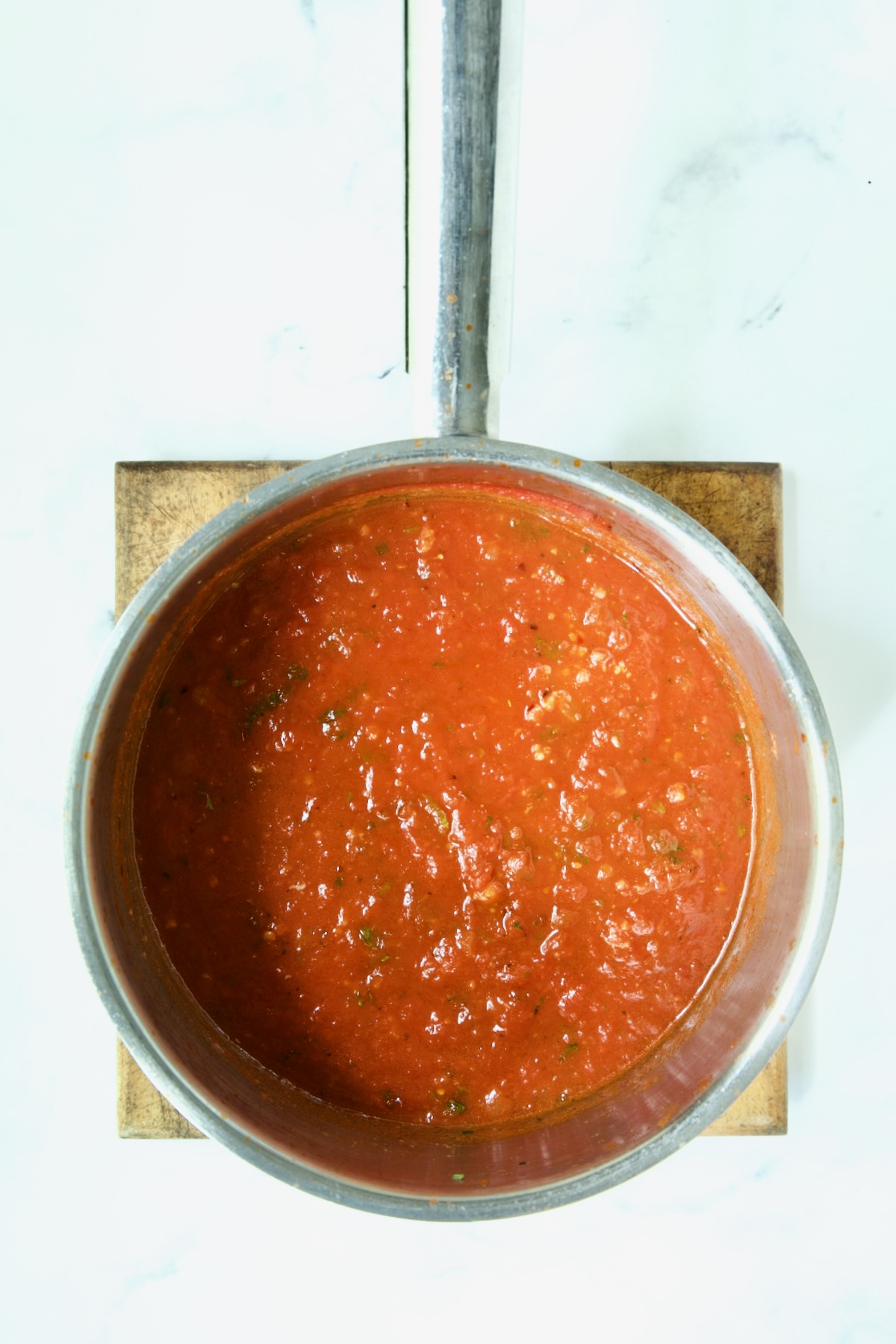 Tomato sauce in stainless steel saucepan on wood trivet.