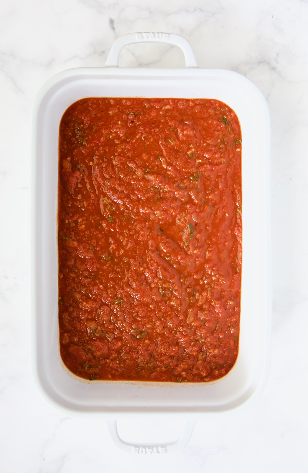 Tomato sauce in the bottom of white rectangular baking dish.