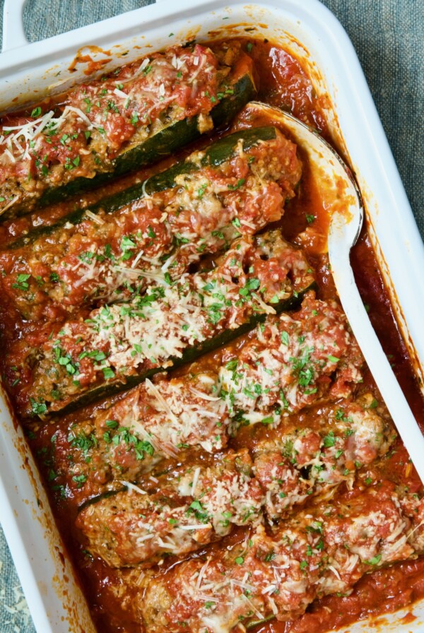 Six Meat-Stuffed Zucchini with Tomato Sauce in white baking dish.