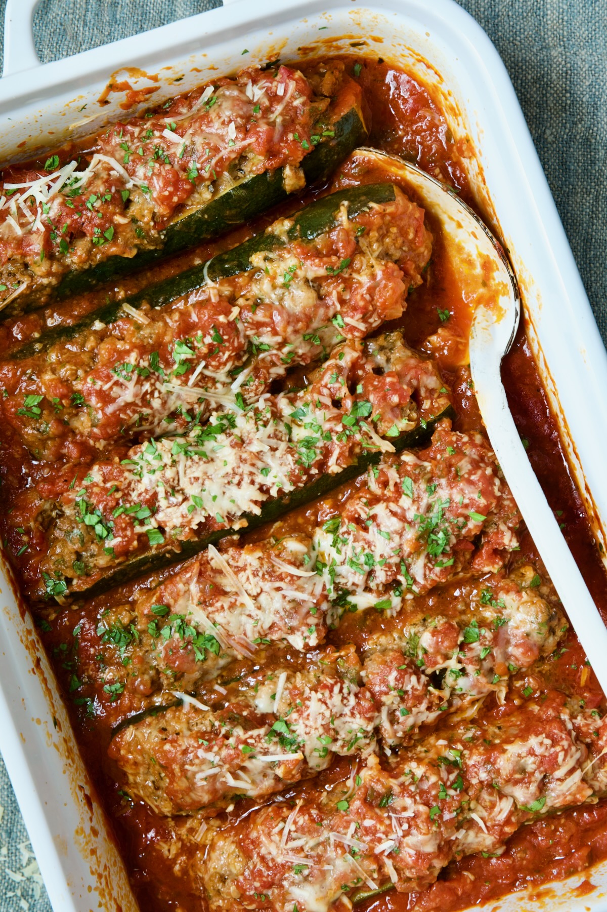 Six Meat-Stuffed Zucchini with Tomato Sauce in white baking dish.