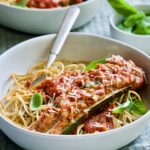 Meat-Stuffed Zucchini with Tomato Sauce in white bowl on blue napkin.
