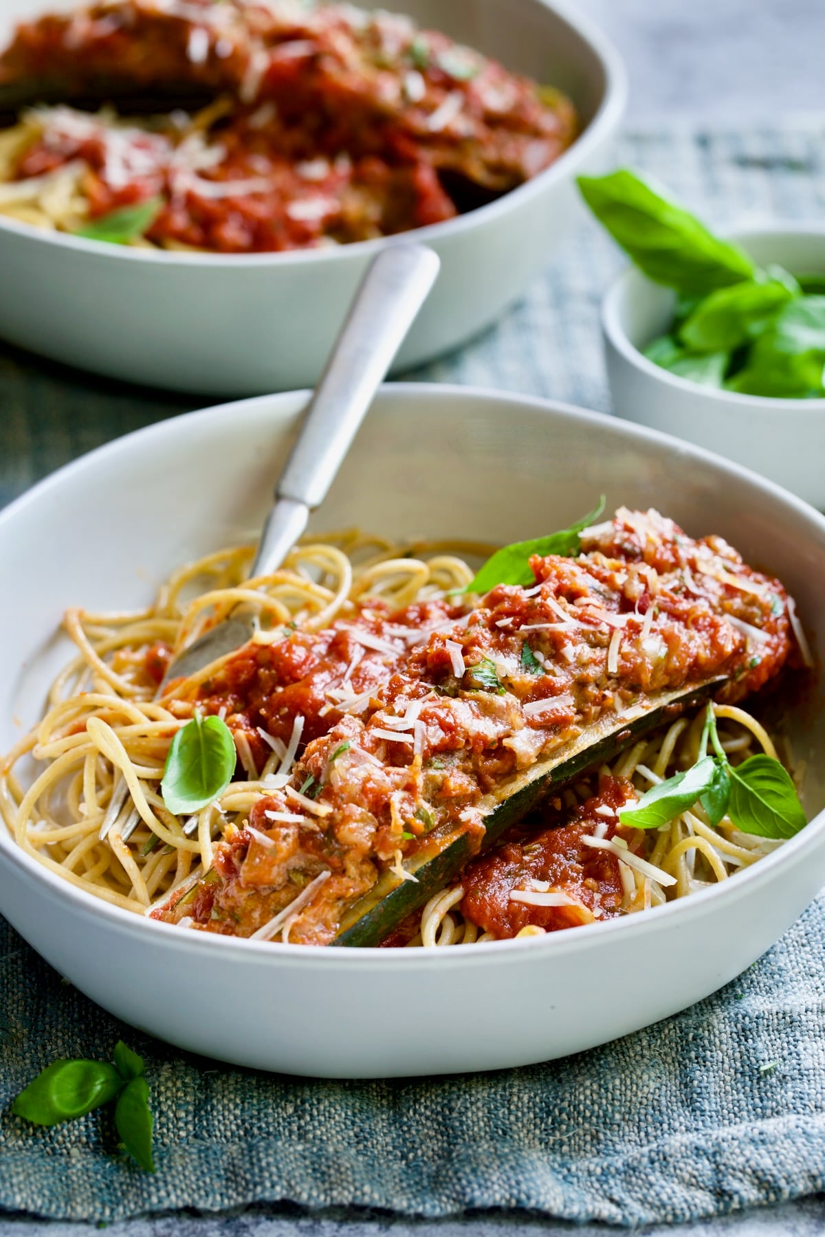 Meat-Stuffed Zucchini with Tomato Sauce in white bowl on blue napkin.
