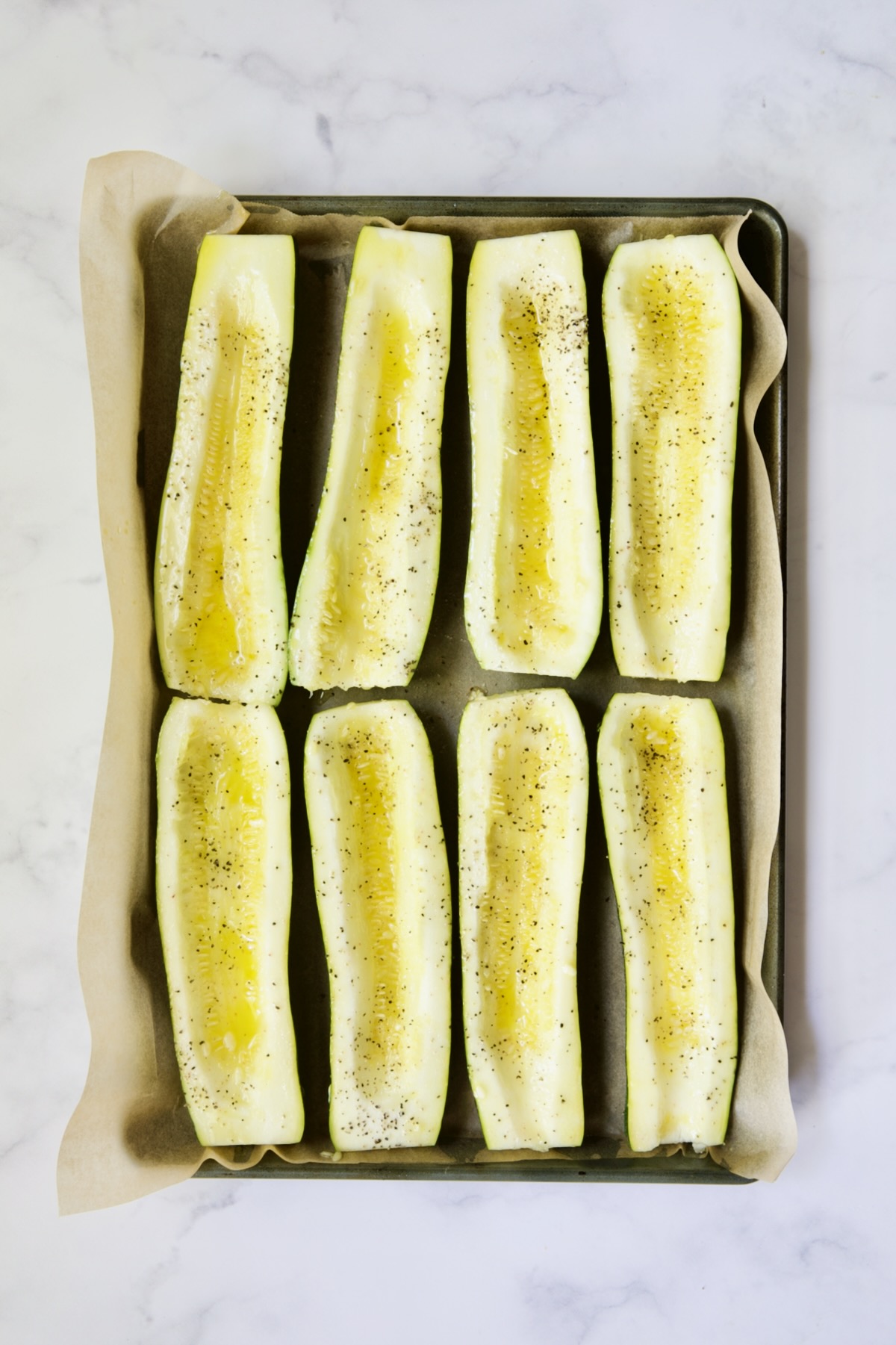 Eight zucchini halves on parchment paper-lined baking sheet before being roasted.