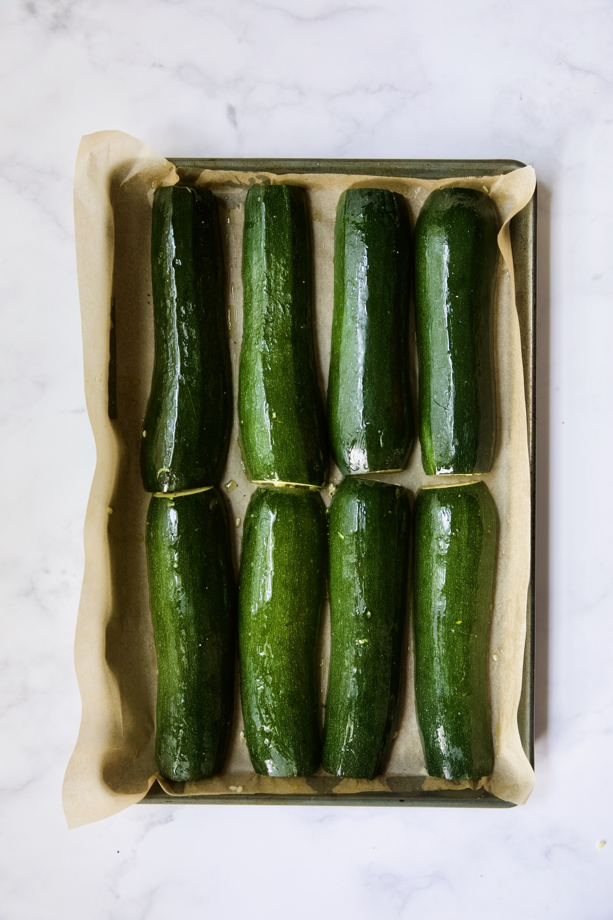 Roasted zucchini halves on parchment-paper lined rimmed baking sheet.