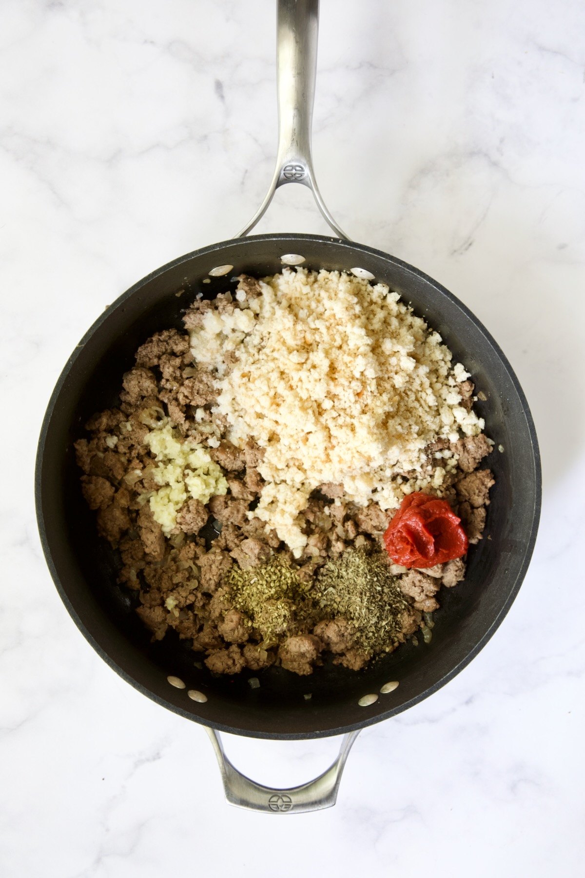 Breadcrumbs, garlic, herbs and tomato paste added to ground beef in nonstick skillet.