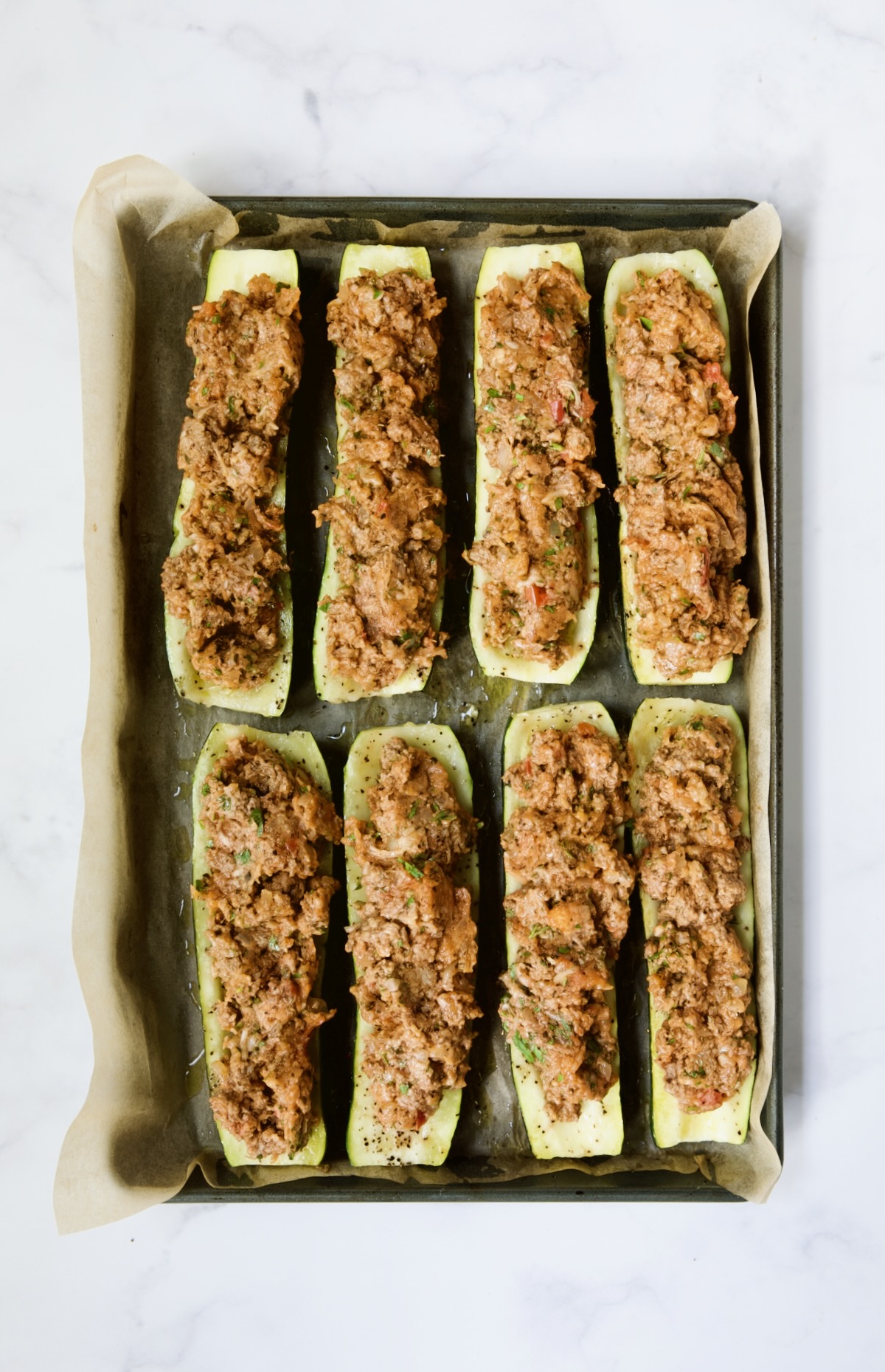 Meat-stuffed zucchini on parchment paper on rimmed baking sheet.