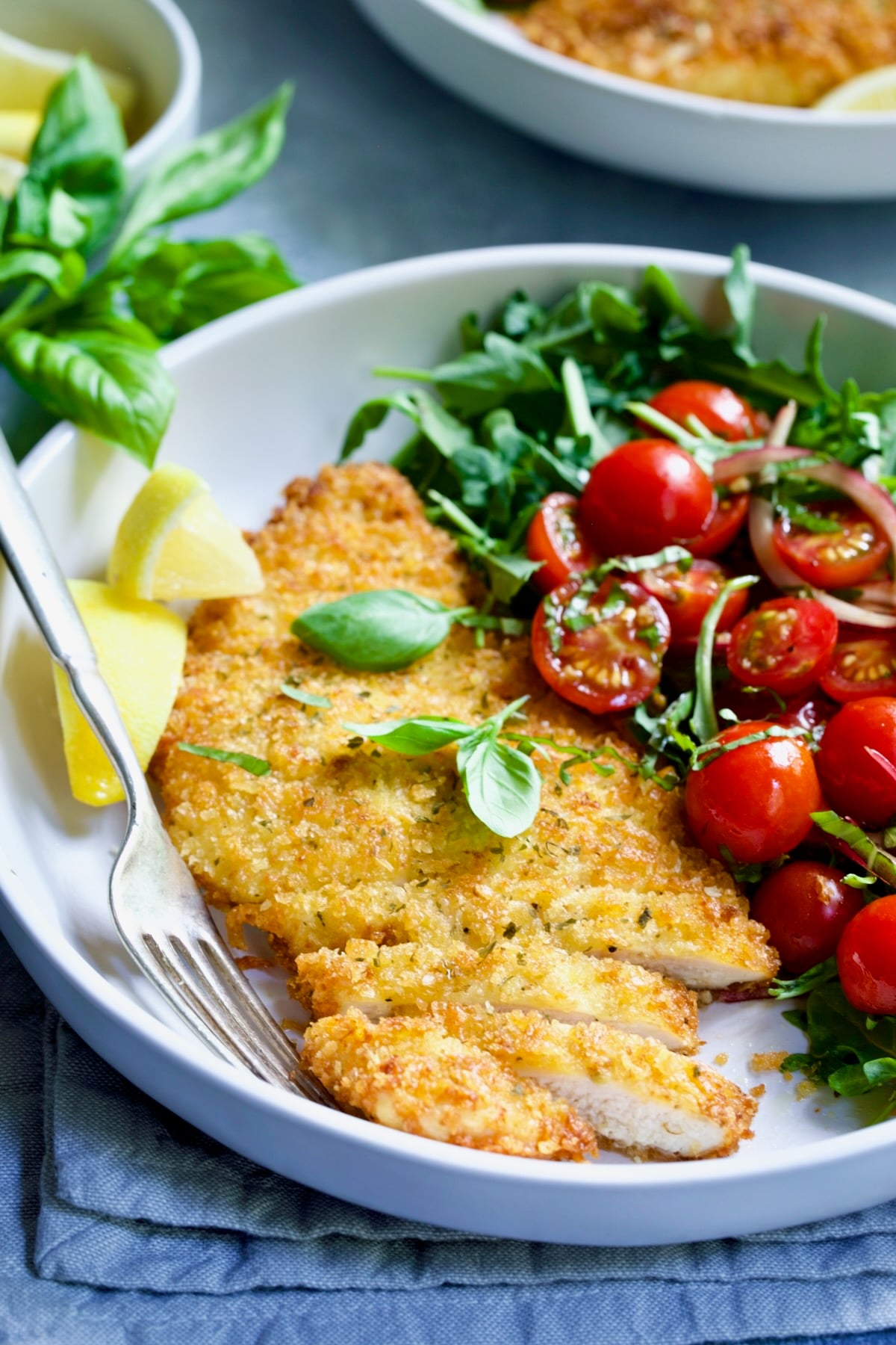 One serving of Chicken Milanese with Arugula and Cherry Tomato Salad in white dish.