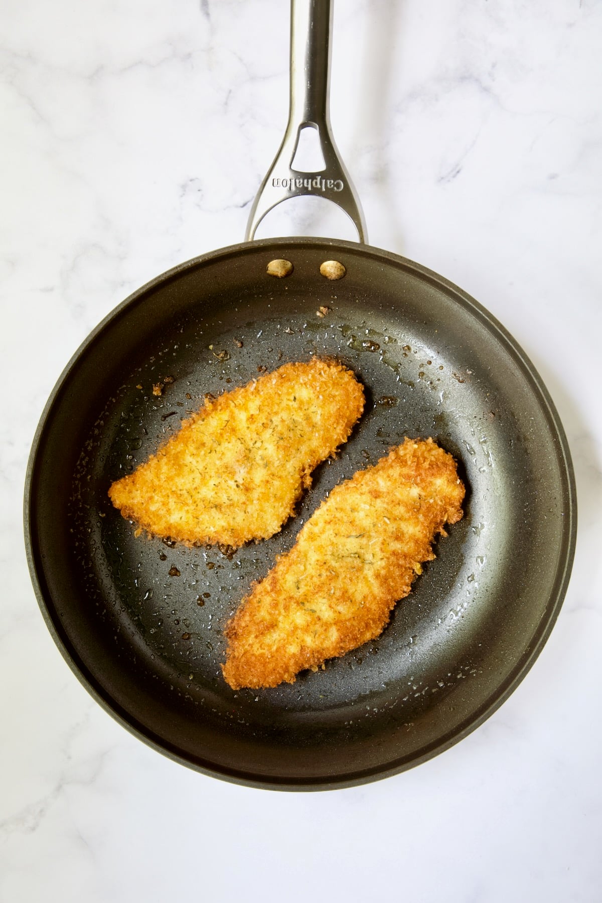 Two fried chicken cutlets in nonstick skillet.