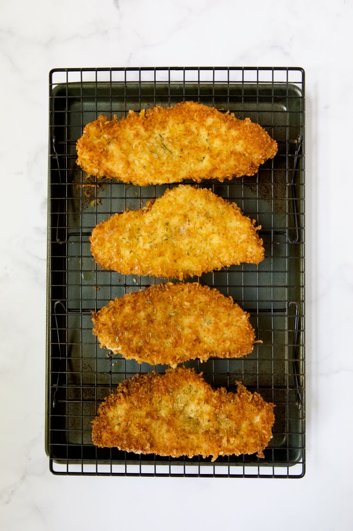 Four pieces of fried chicken cutlets on cooling rack set over a baking sheet.