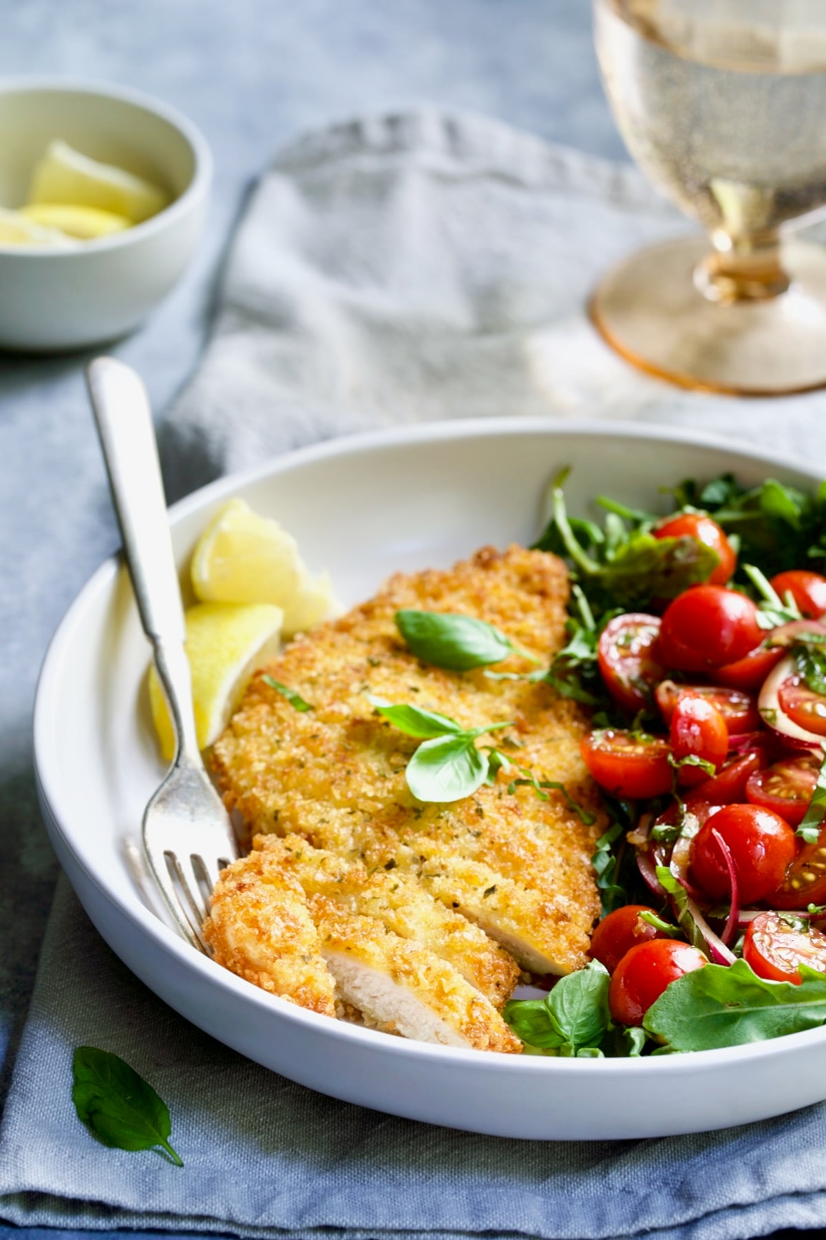 One serving of Chicken Milanese with Arugula and Cherry Tomato Salad in white bowl.