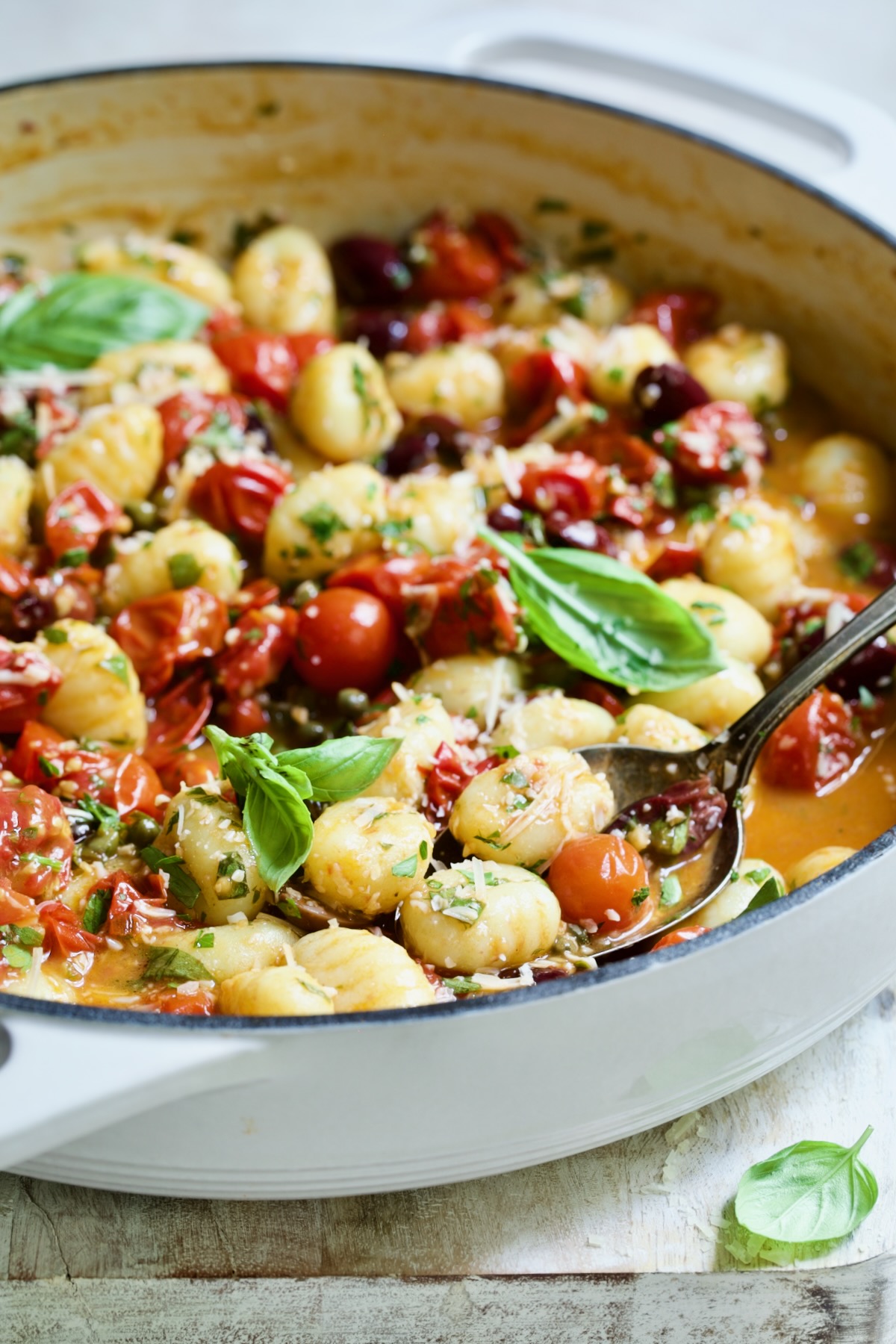Gnocchi with Cherry Tomato Puttanesca Sauce in white enamel cast iron skillet with some on serving spoon.