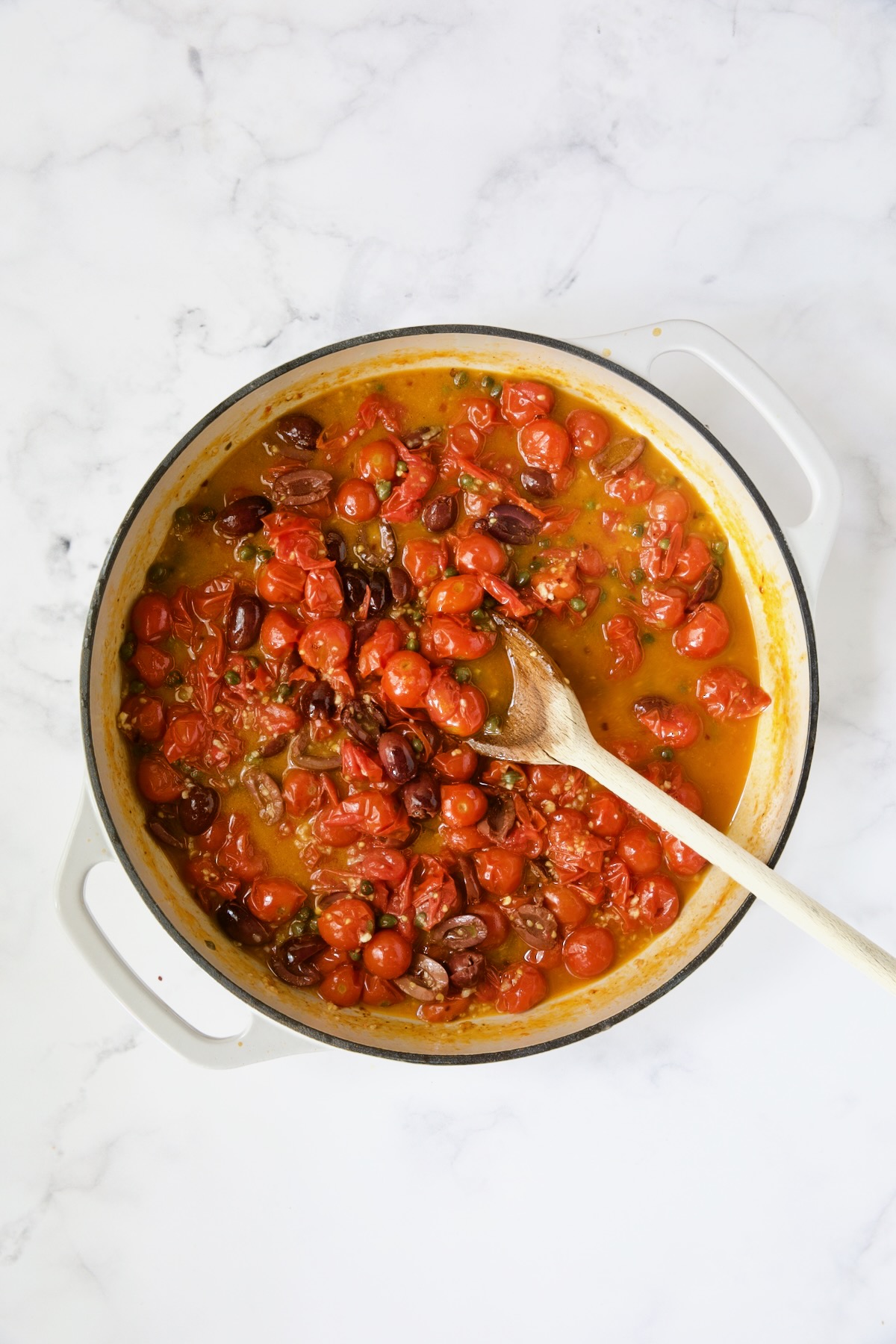 Cherry tomatoes and olives being stirred with wooden spoon.