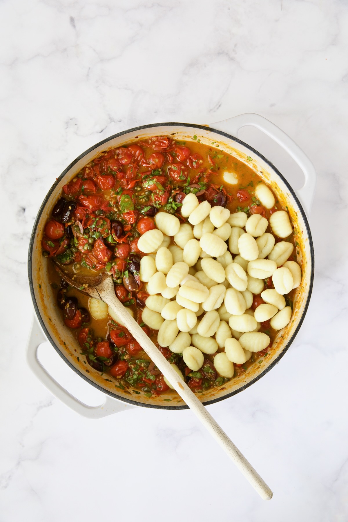 Puttanesca sauce in white enamel cast iron skillet with gnocchi added but not stirred in.