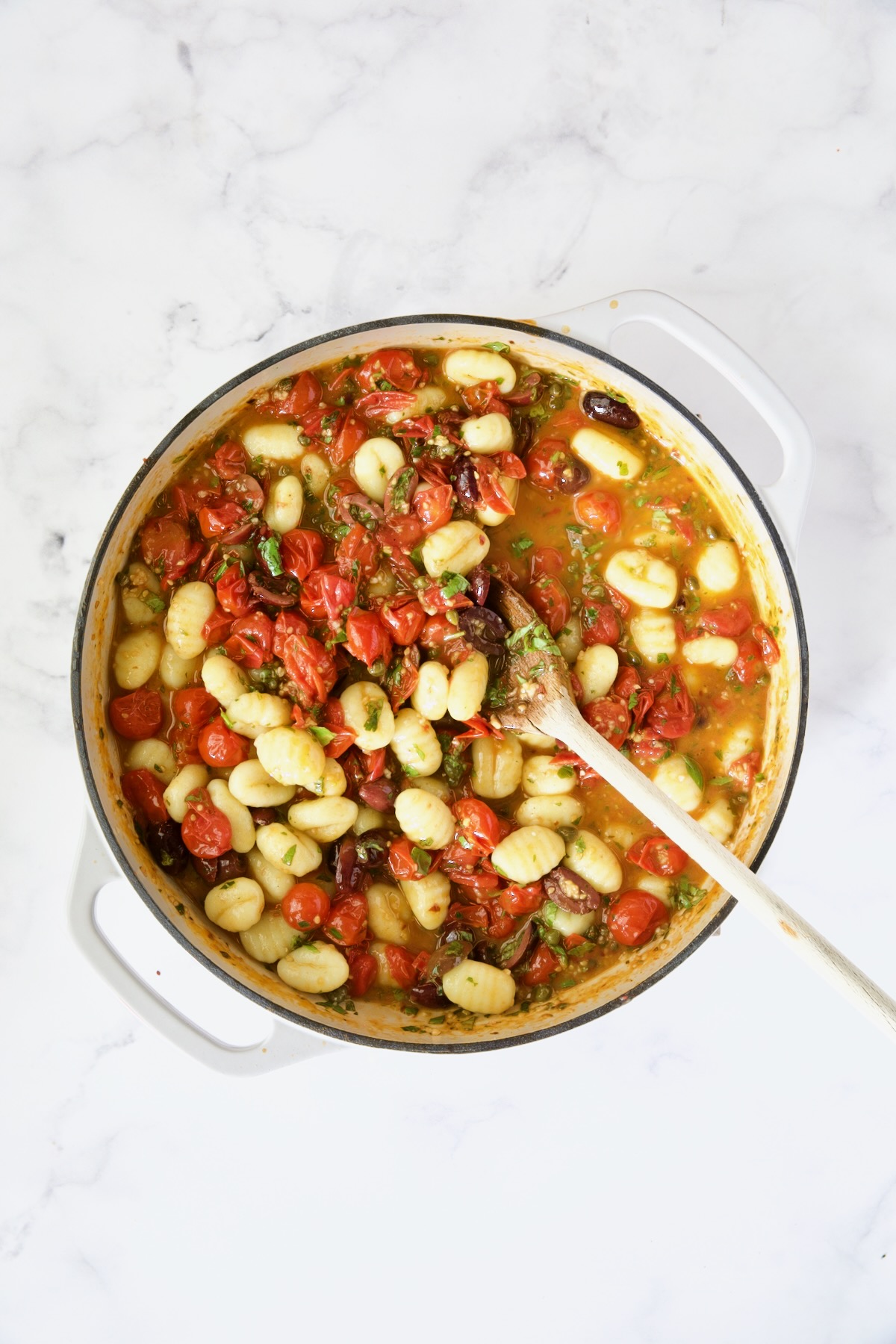 Gnocchi with the puttanesca sauce in white enamel cast iron skillet.