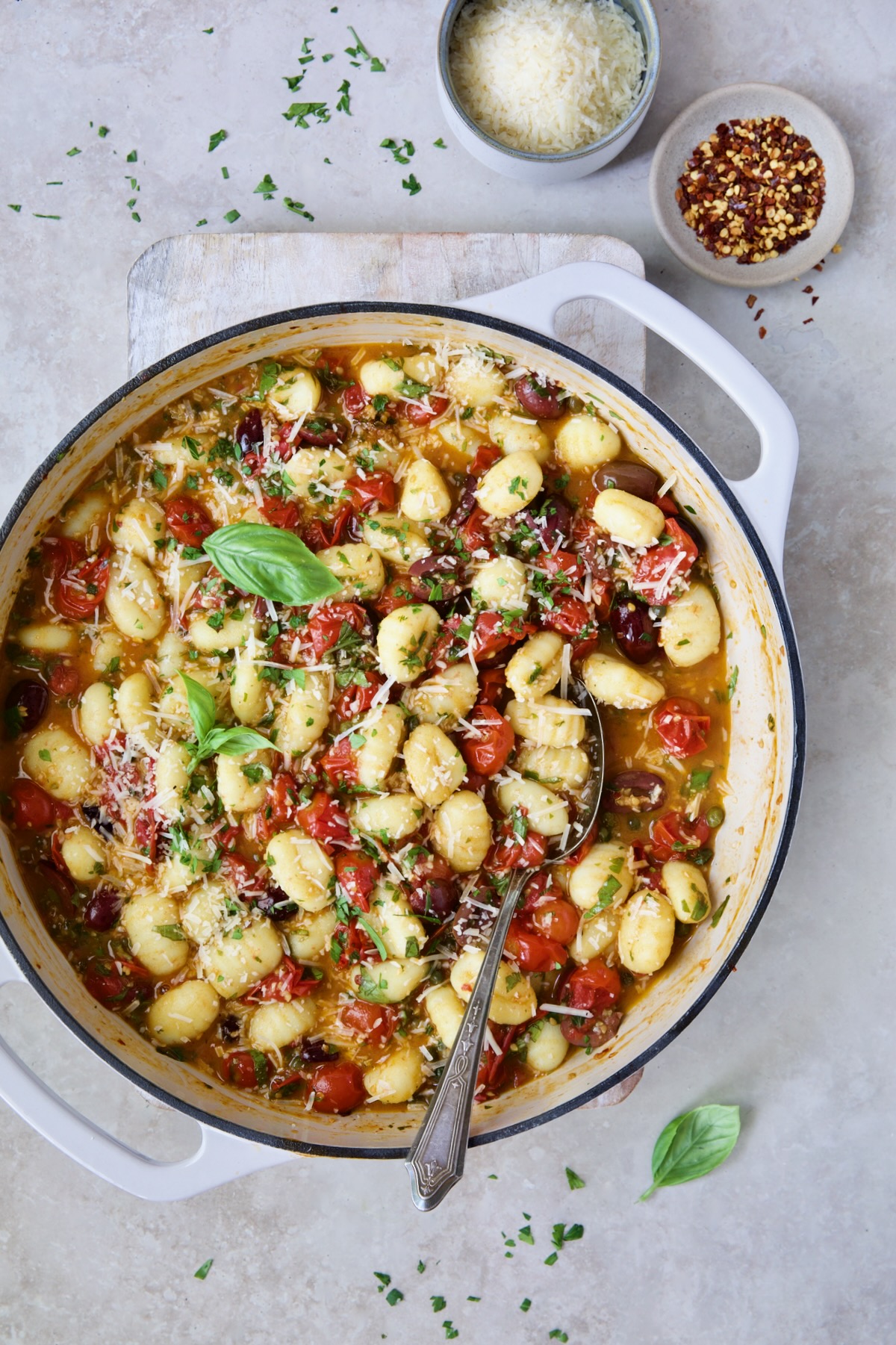 Gnocchi with Cherry Tomato Puttanesca Sauce in white enamel cast iron skillet on white board.