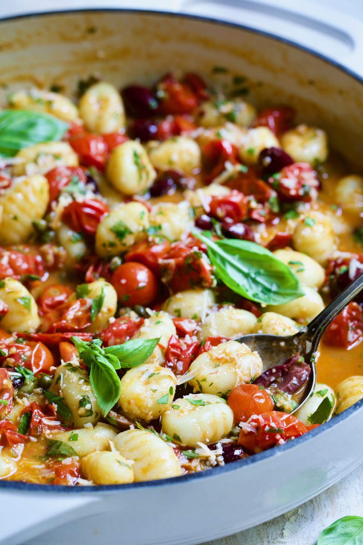 Gnocchi with Cherry Tomato Puttanesca Sauce in white enamel cast iron skillet with serving spoon scooping some up.