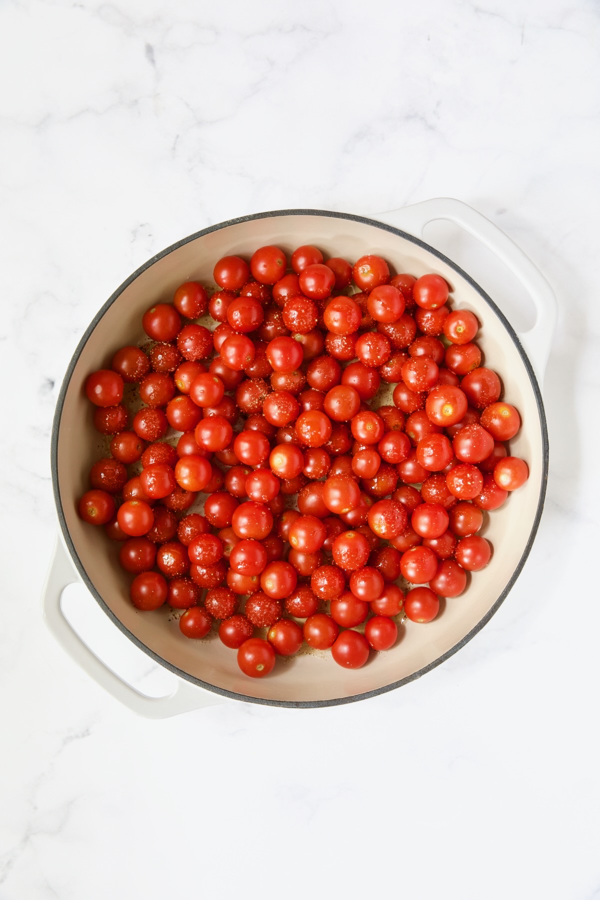 Uncooked cherry tomatoes in white enamel cast iron skillet.
