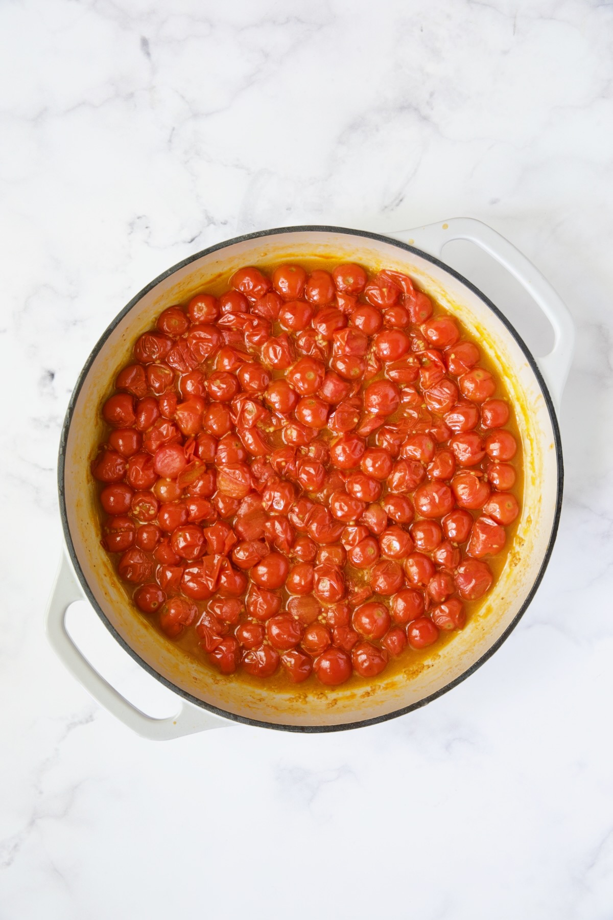 Cooked cherry tomatoes in white enamel cast iron skillet.