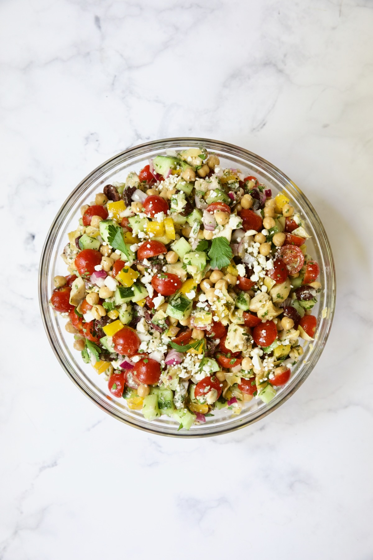 Chopped salad in glass bowl on white marble background.