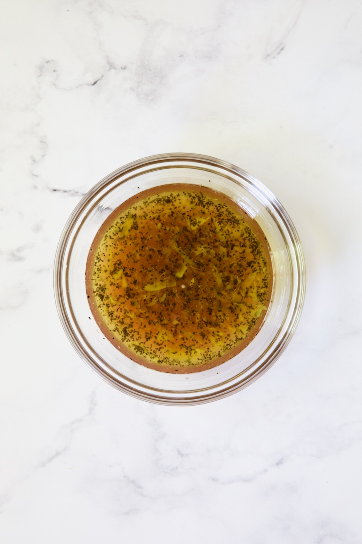 Vinaigrette in glass bowl on white marble background.