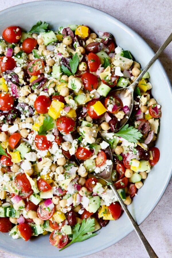 Mediterranean Chopped Salad with Chickpeas in blue bowl with serving spoons.