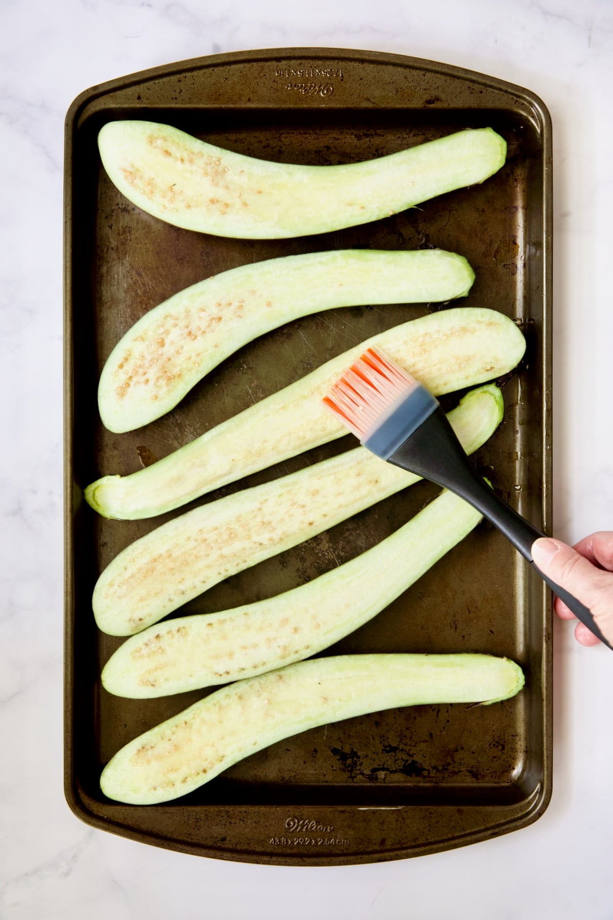 Six Japanese eggplant halves being brushed with oil.