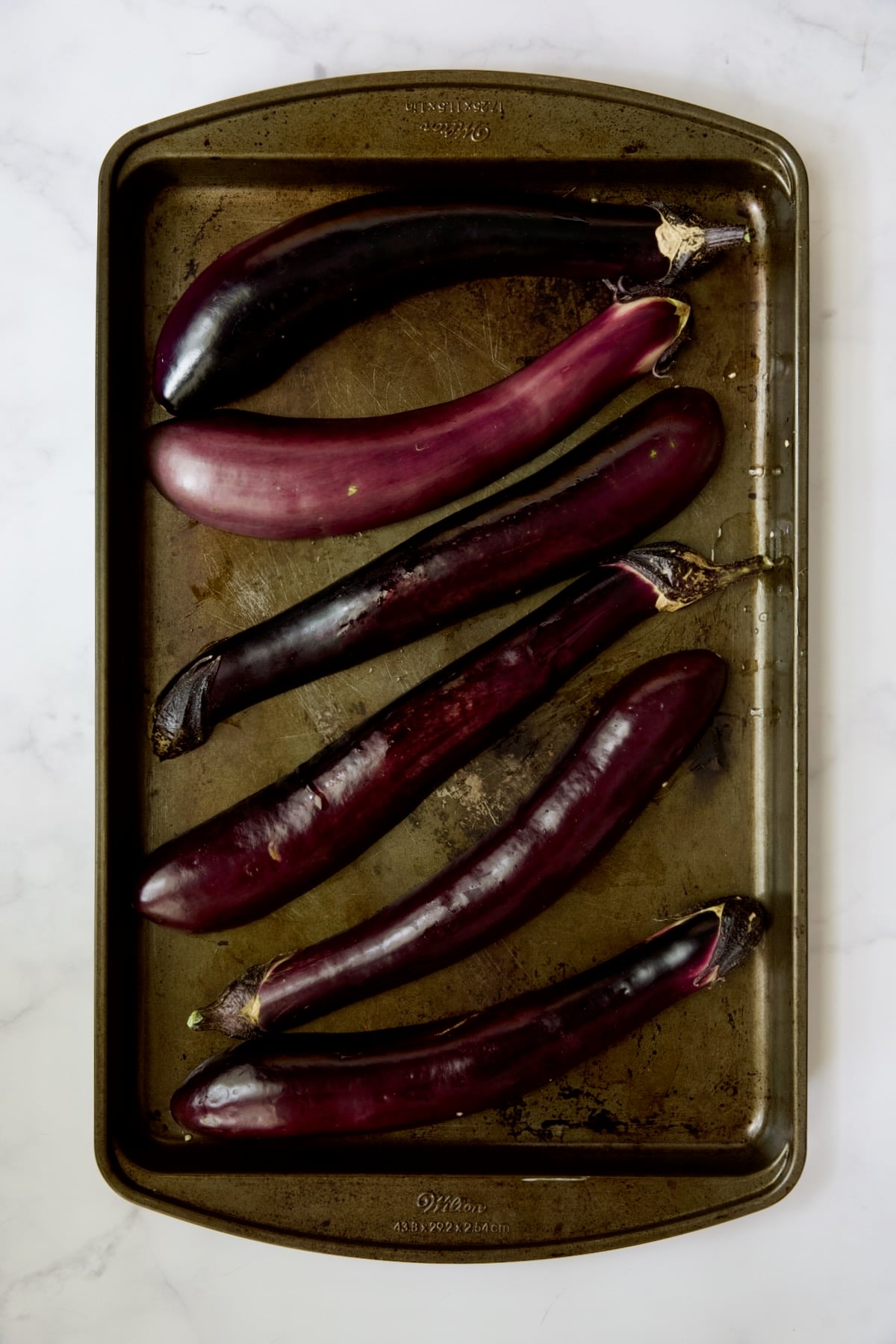 Six Japanese eggplant halves on rimmed baking sheet.