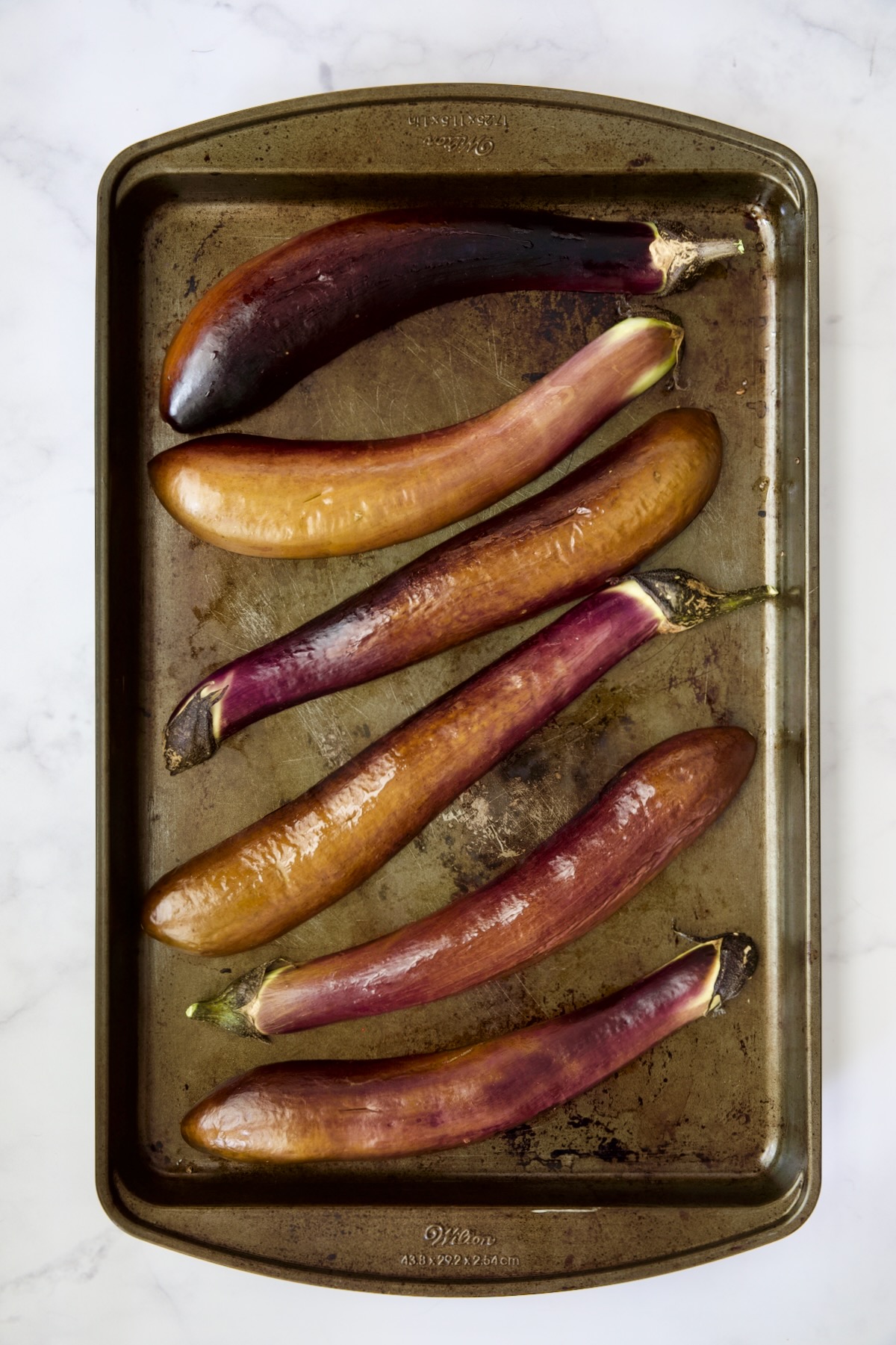 Six baked Japanese eggplant halves on rimmed baking sheet.